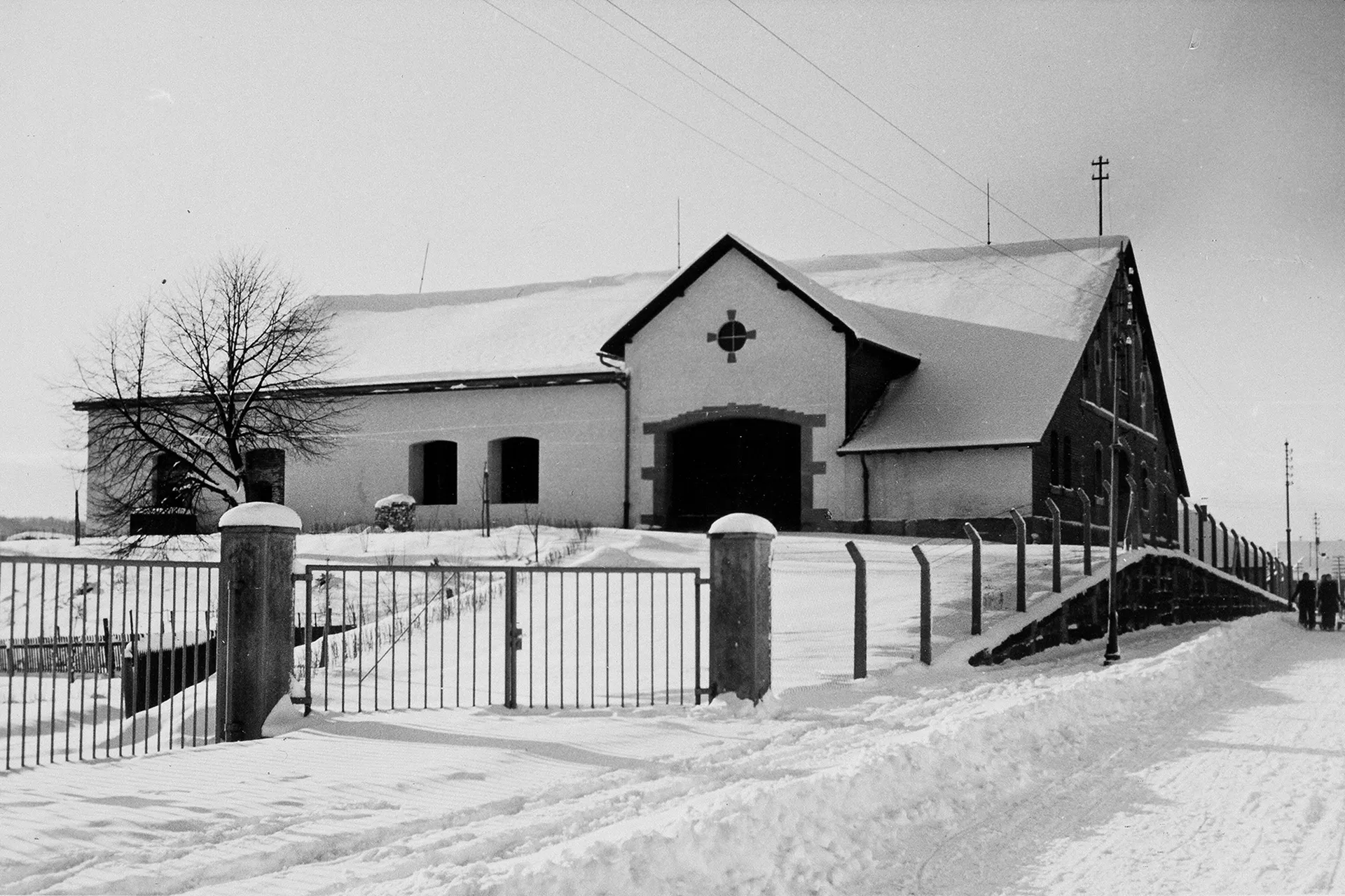 Ein längliches Gebäude an einer Straße in einer Winterlandschaft mit Schnee; Schwarz-Weiß-Foto.