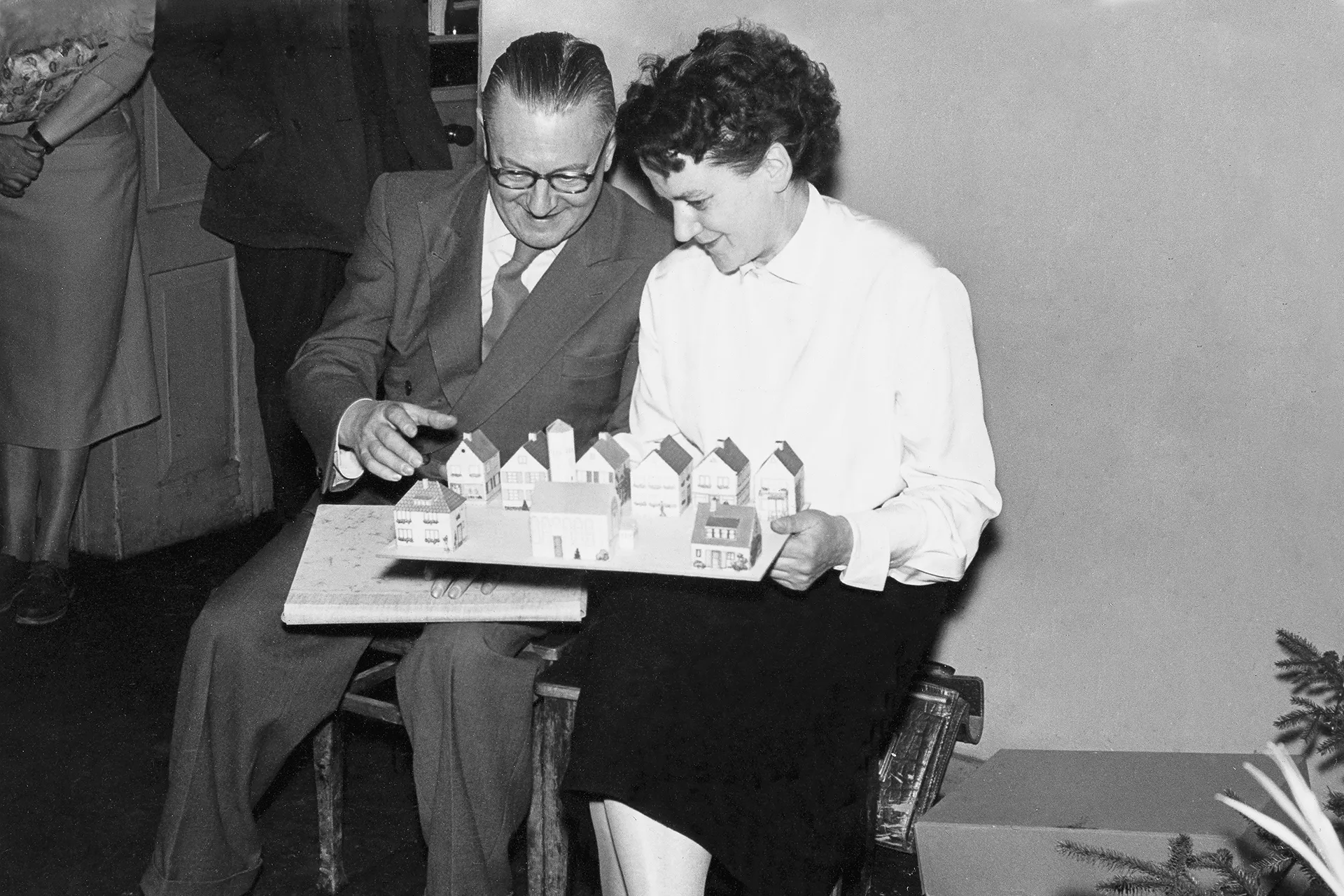 Ein sitzendes Paar, Eugen und Luise Habermaaß, betrachtet ein Häusermodell, das es auf dem Schoß hält; Schwarz-Weiß-Foto.