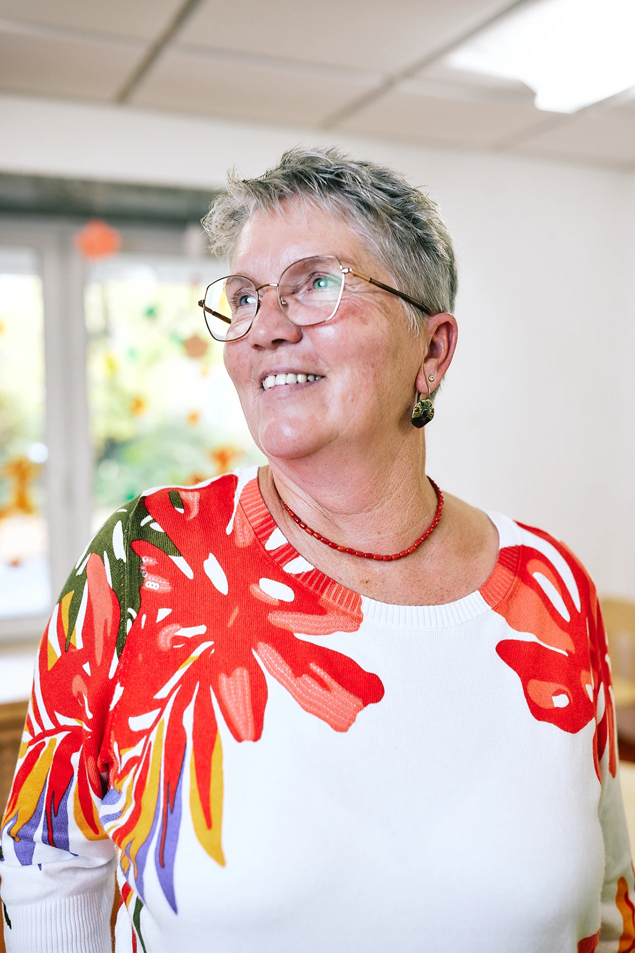 Portraitfoto von Beatrix Hirsch. Sie hat kurzes, blondes Haar, trägt eine Brille und einen Pullover mit floralem Muster.