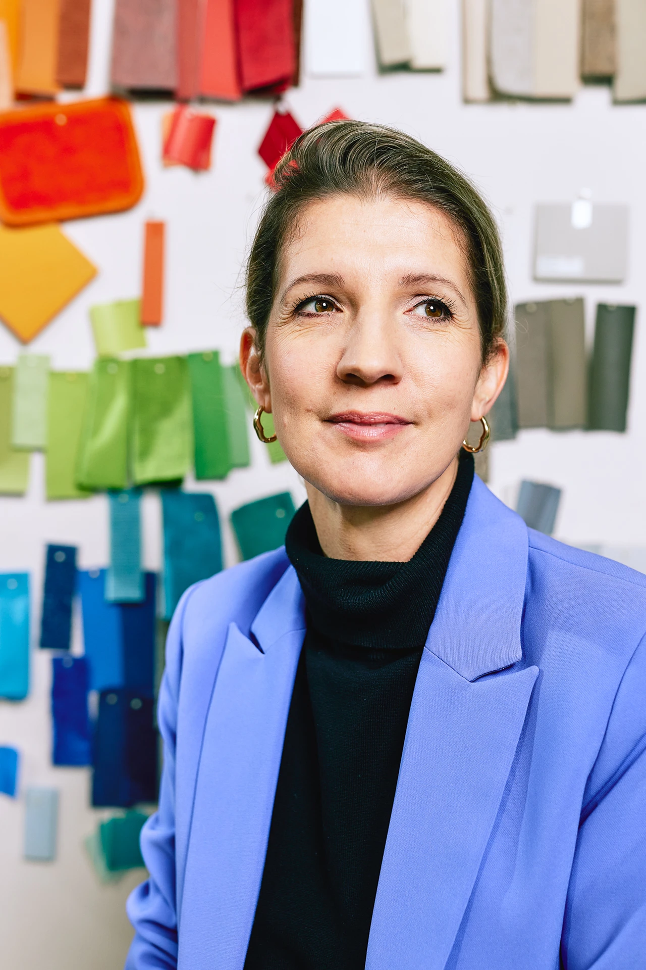 Portraitfoto von Lisa Werner. Sie trägt einen violetten Blazer und sitzt vor einer Wand mit Stoffmustern.