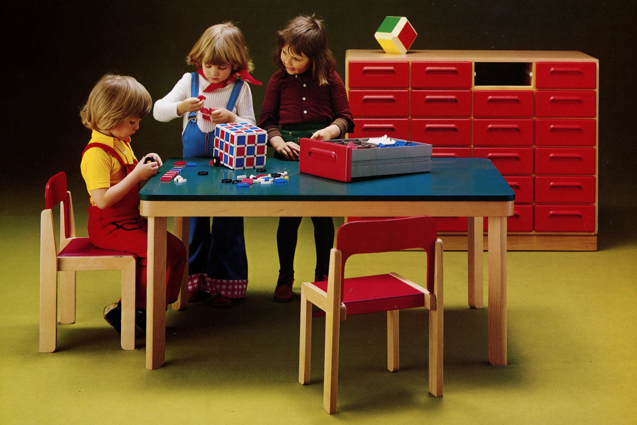 Kinder sitzen und stehen an einem Tisch und spielen.