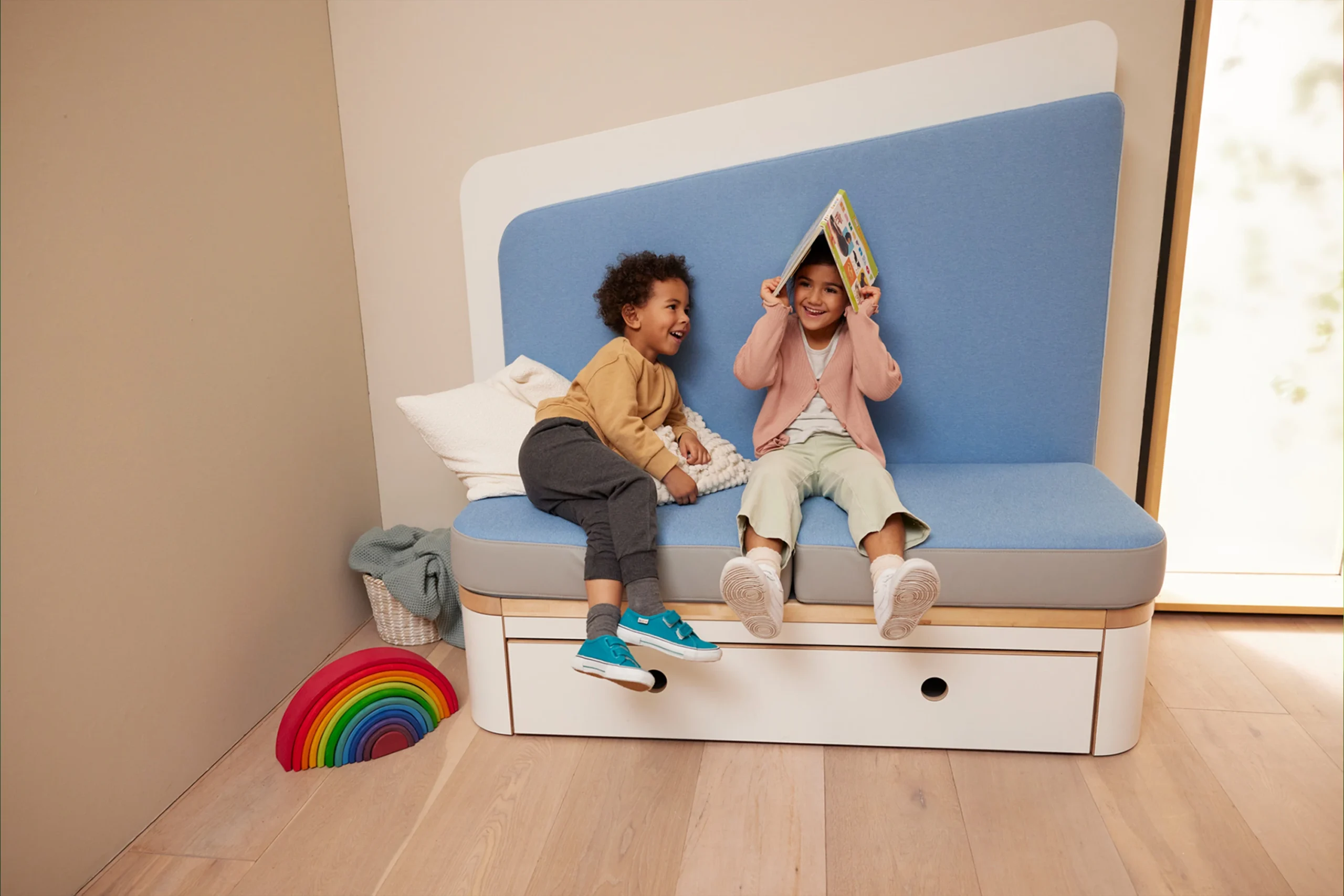 Zwei Kinder sitzen auf einem sofaartigen Möbelstück der Firma Wehrfritz.