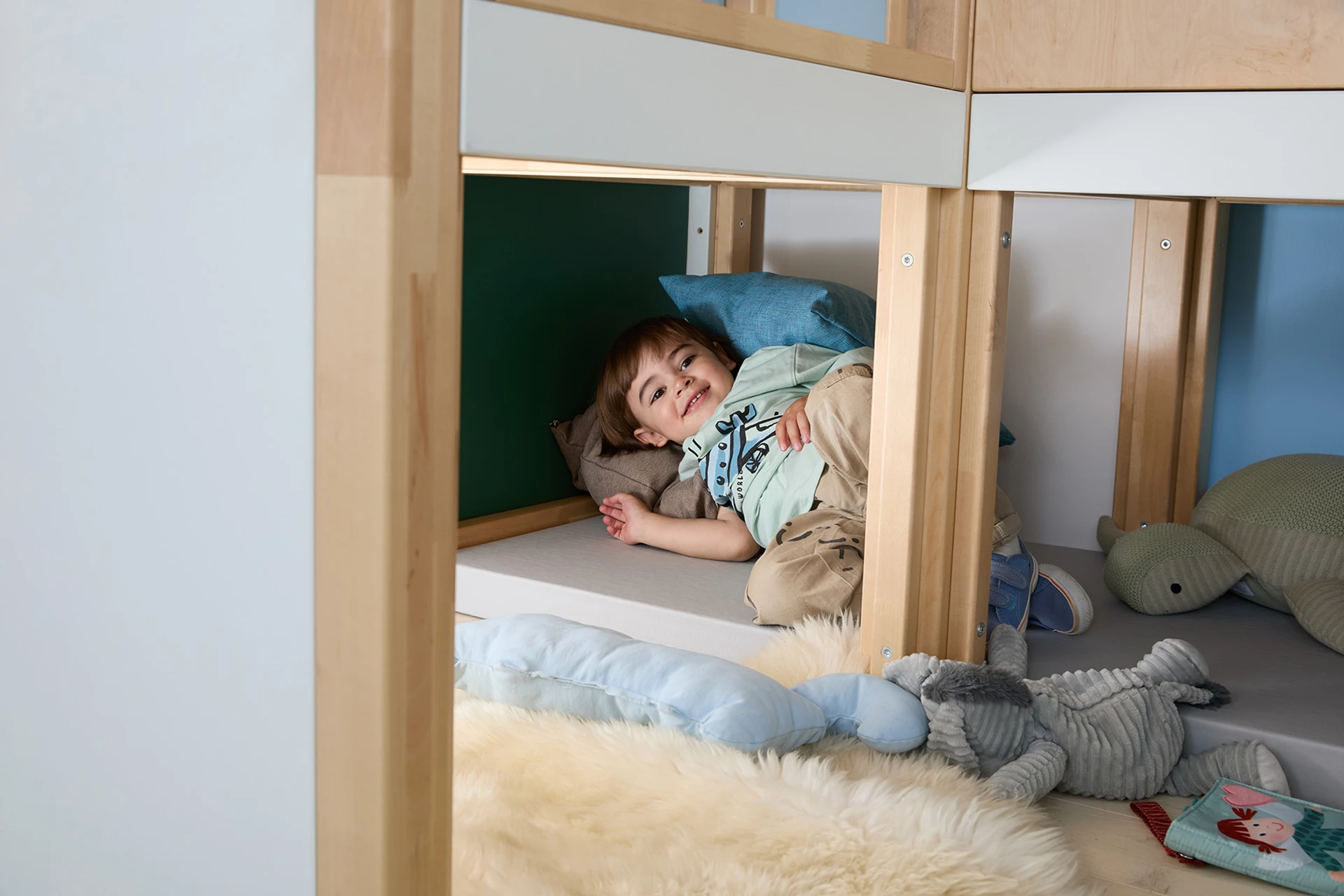 Ein Kind liegt in der unteren Ebene des Möbelstücks Gemino wie in einer Höhle.