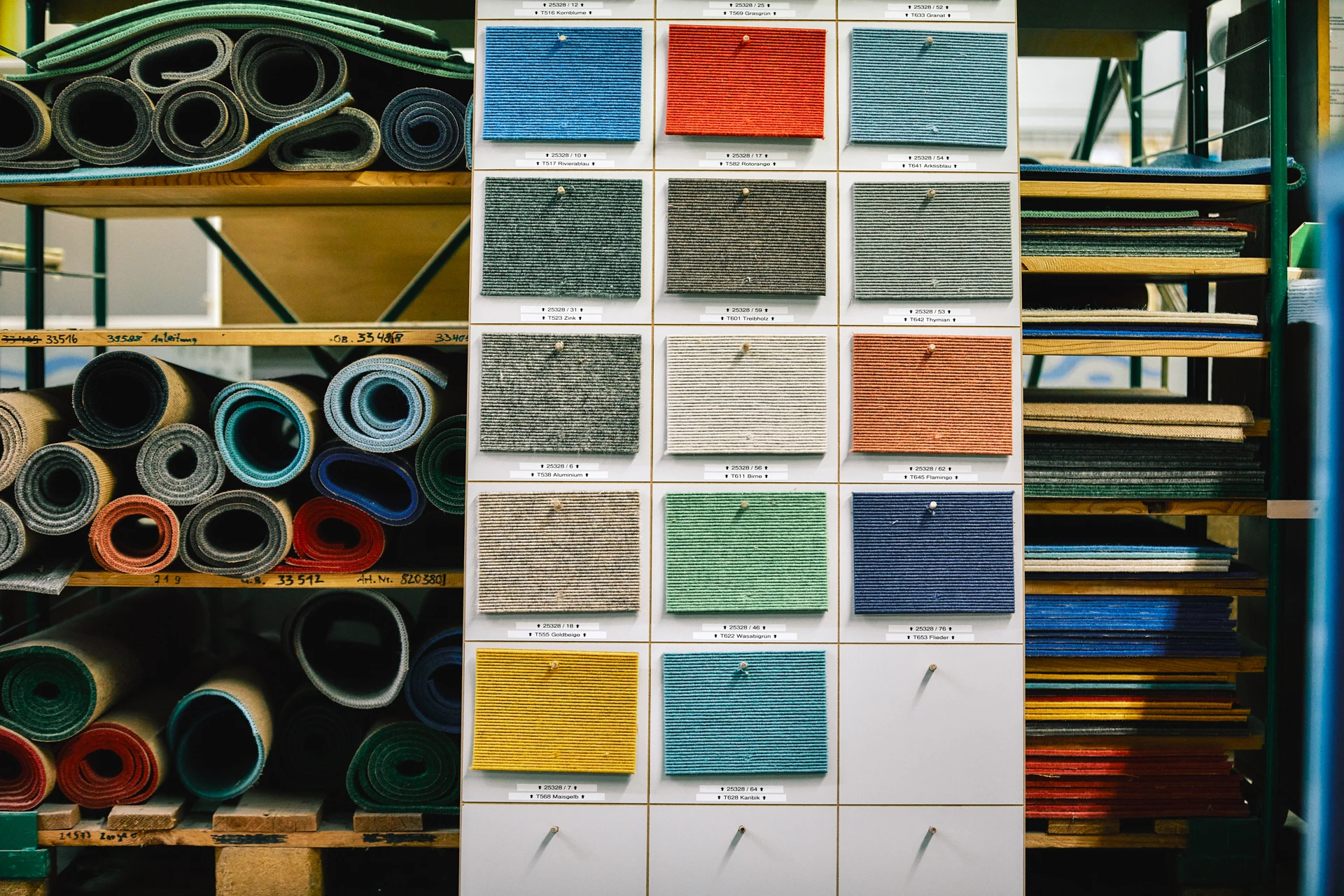 Bunte Stoffmuster hängen an einer Tafel bei einem Lagerregal.