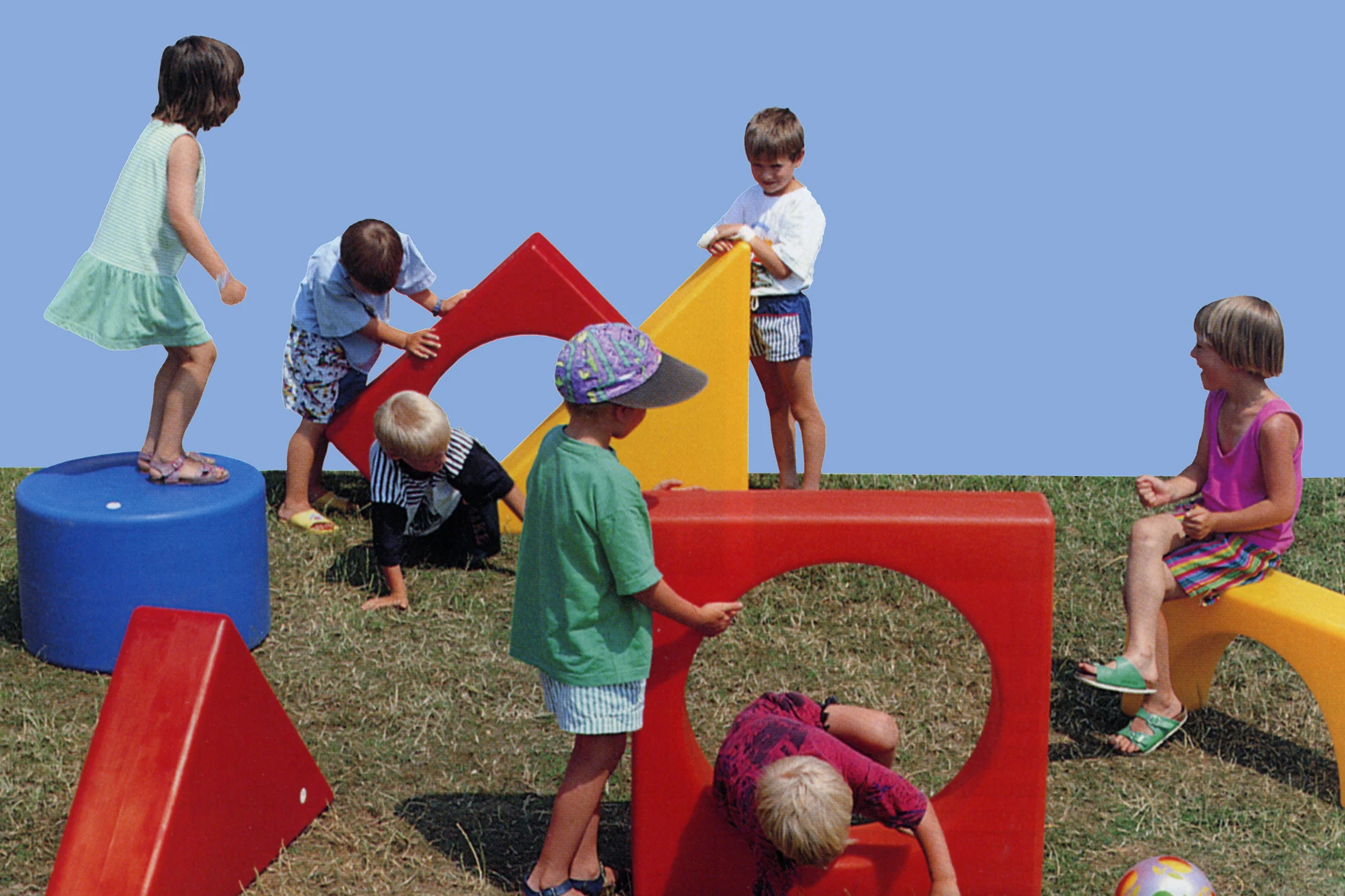 Kinder spielen im Freien mit bunten Spielmöbeln in verschiedenen geometrischen Formen.