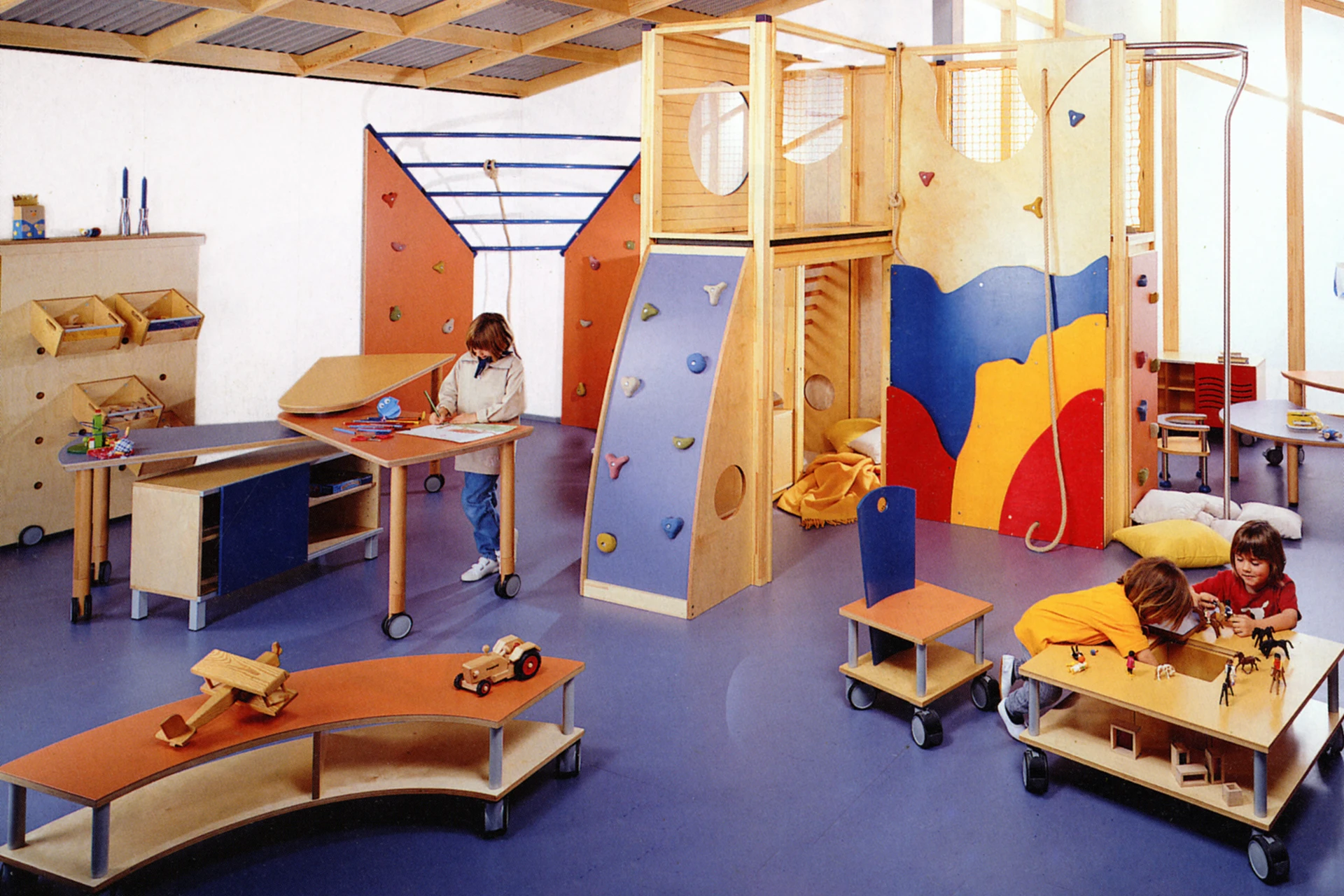 Kindergartenraum, der mit Möbeln des Systems move-upp der Firma Wehrfritz eingerichtet ist. Zu sehen sind unter anderem eine Kletterwand, Tische und Regale auf Rollen.